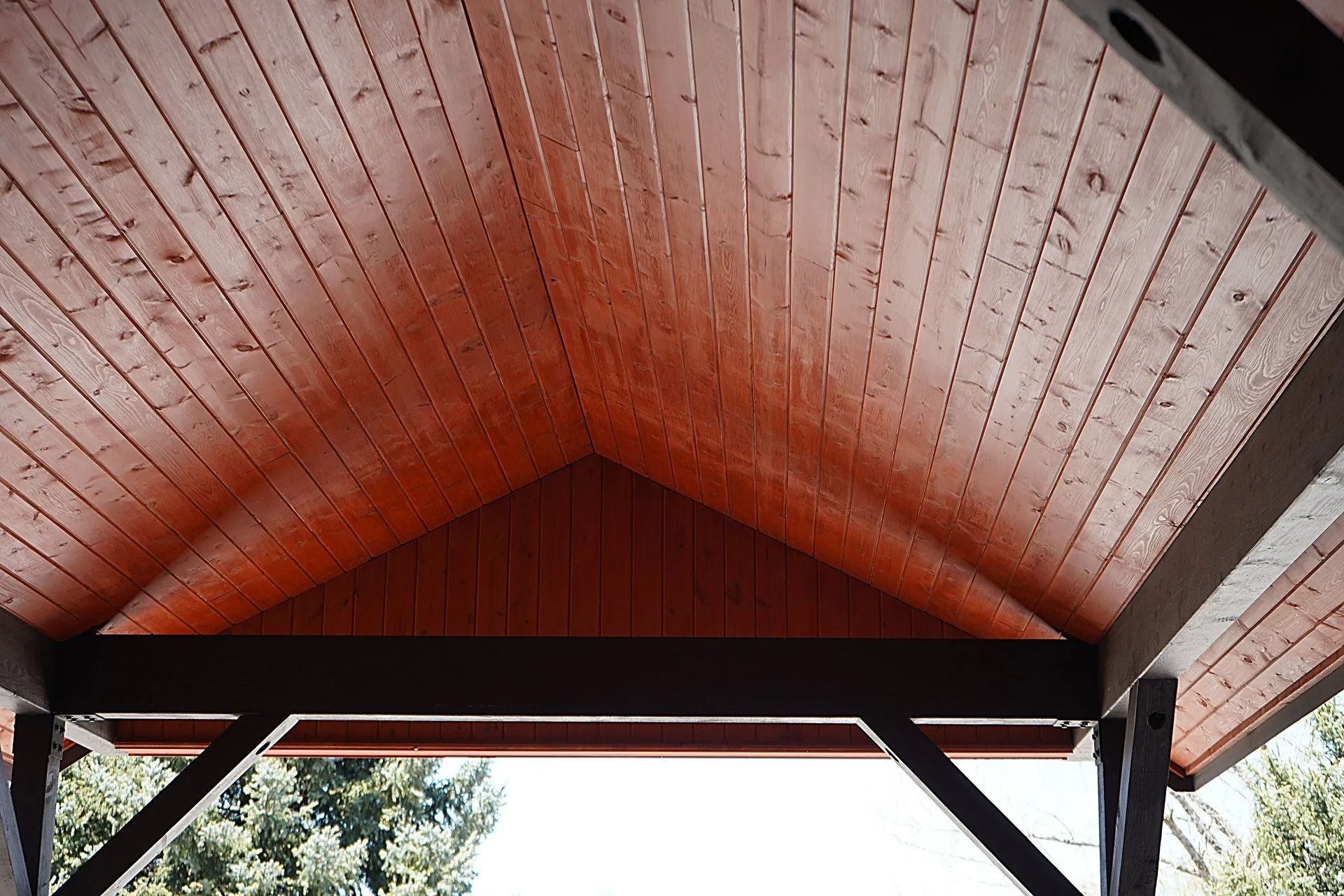 A close-up of a vaulted, warm-toned wooden ceiling featuring plank paneling and dark brown supporting beams.