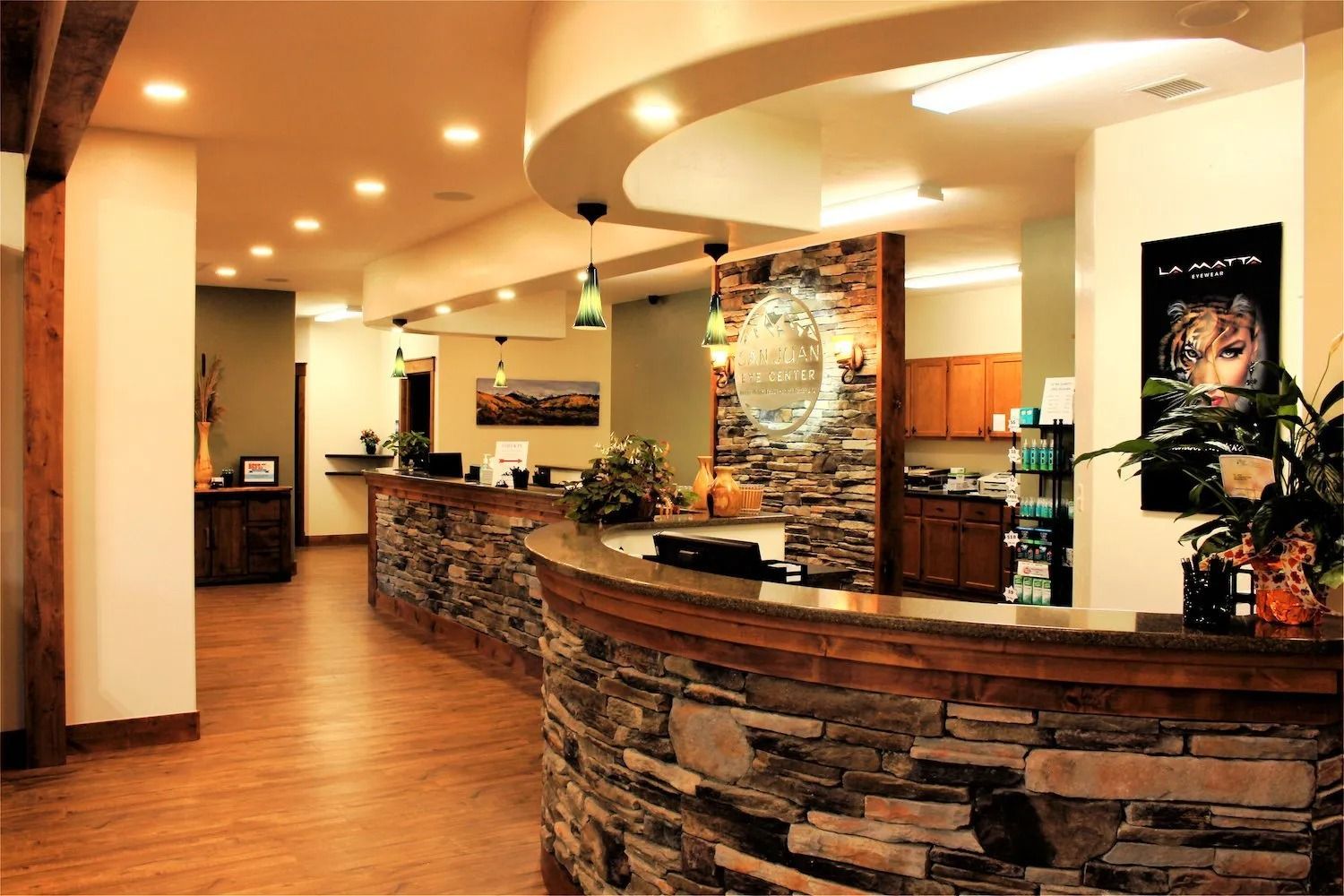 A spacious medical office reception area with a curved stone front desk, wood flooring, and warm recessed lighting.