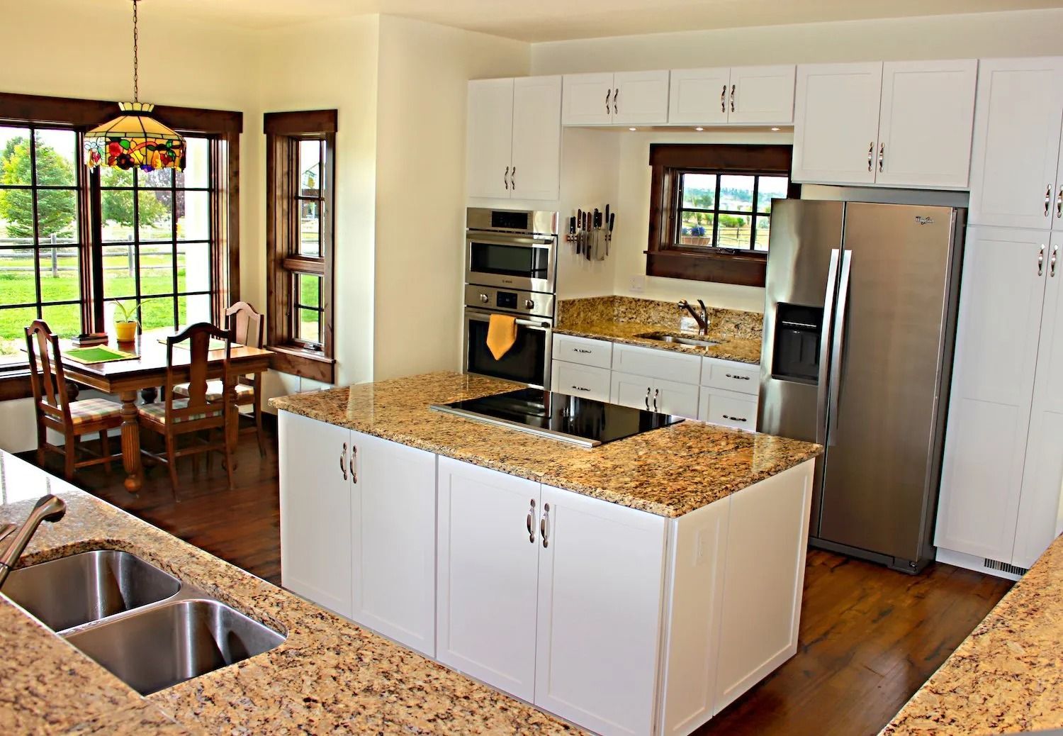 A kitchen with white cabinets, granite countertops, a center island with a cooktop, and a stainless steel refrigerator.