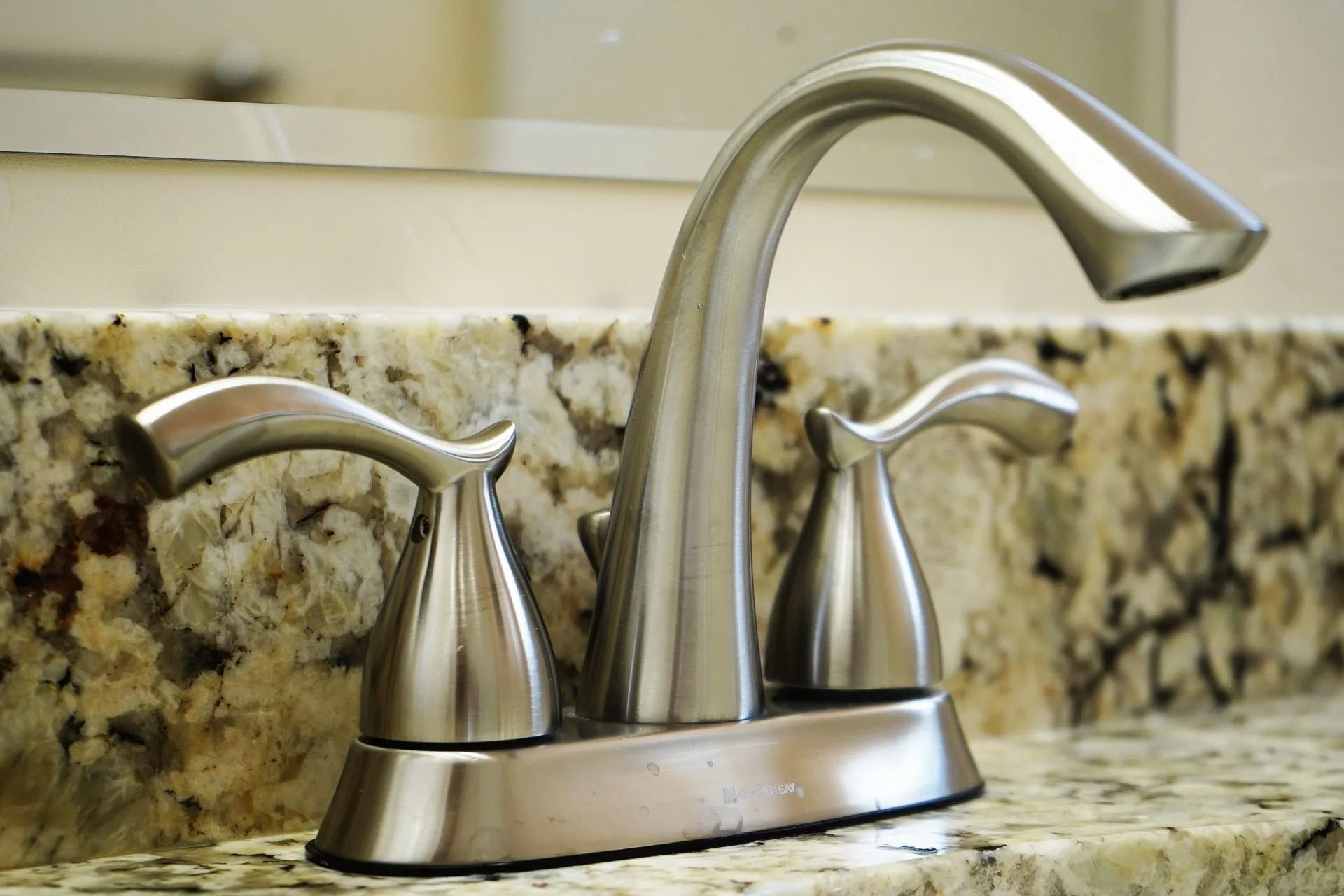 A modern, brushed-nickel bathroom faucet set on a speckled granite countertop with a mirror in the background.