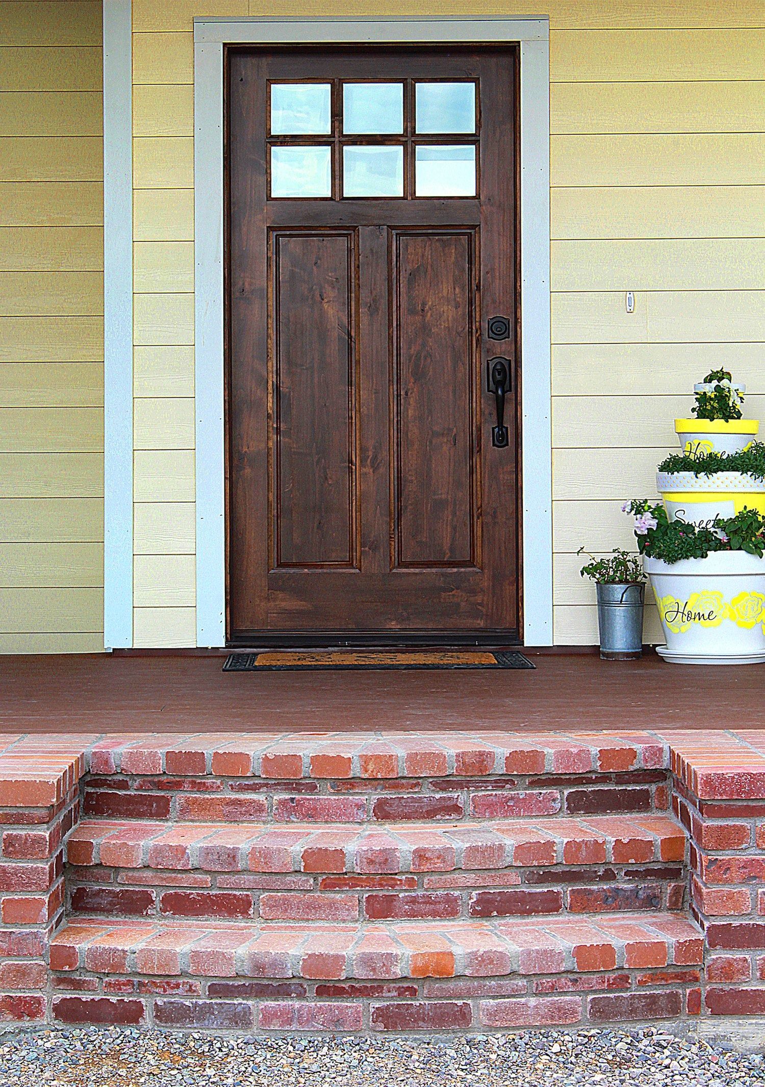 A dark wood door with six glass panes sits on a porch with brick steps and a tiered white planter.