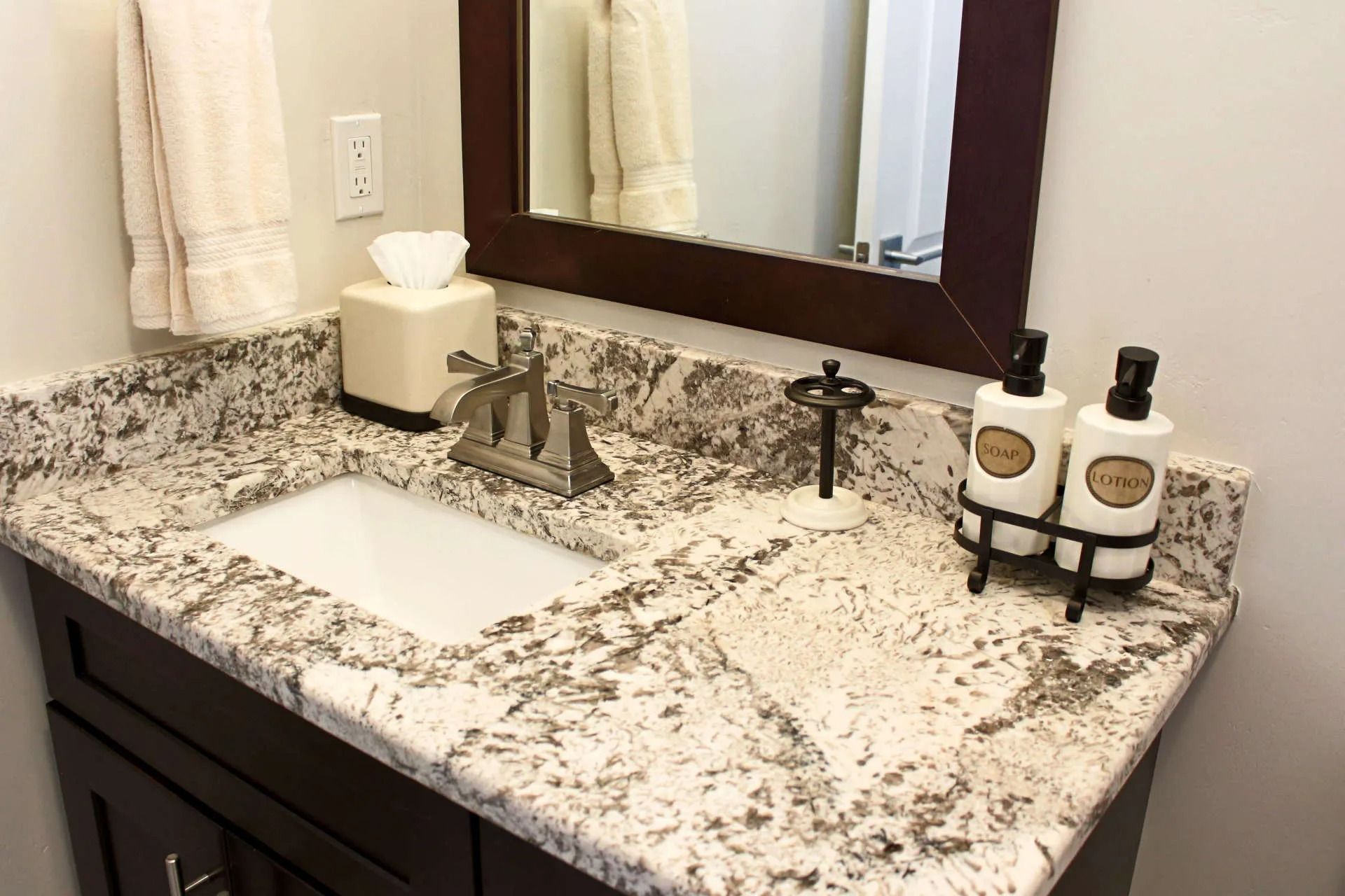 Bathroom vanity with speckled granite countertop, white sink, dark wood cabinet, mirror, and white soap dispensers.