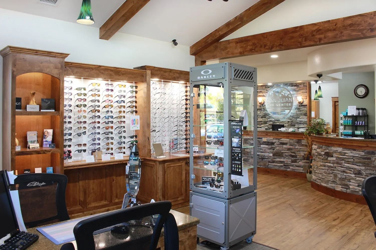 Eye doctor's office interior with wooden display shelves of glasses, a central glass case, and a stone-front reception desk.