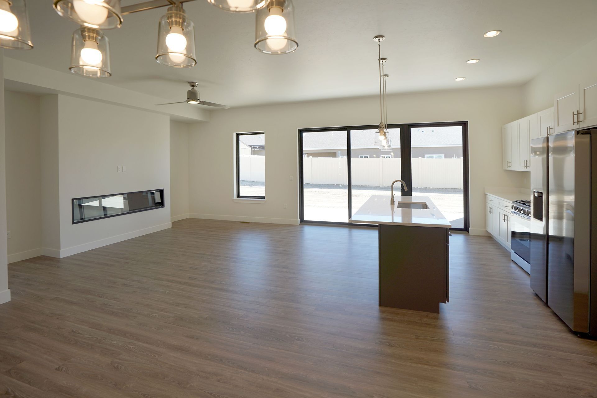 Modern open-plan kitchen and living area with wood floors, a central island, stainless steel fridge, and fireplace.