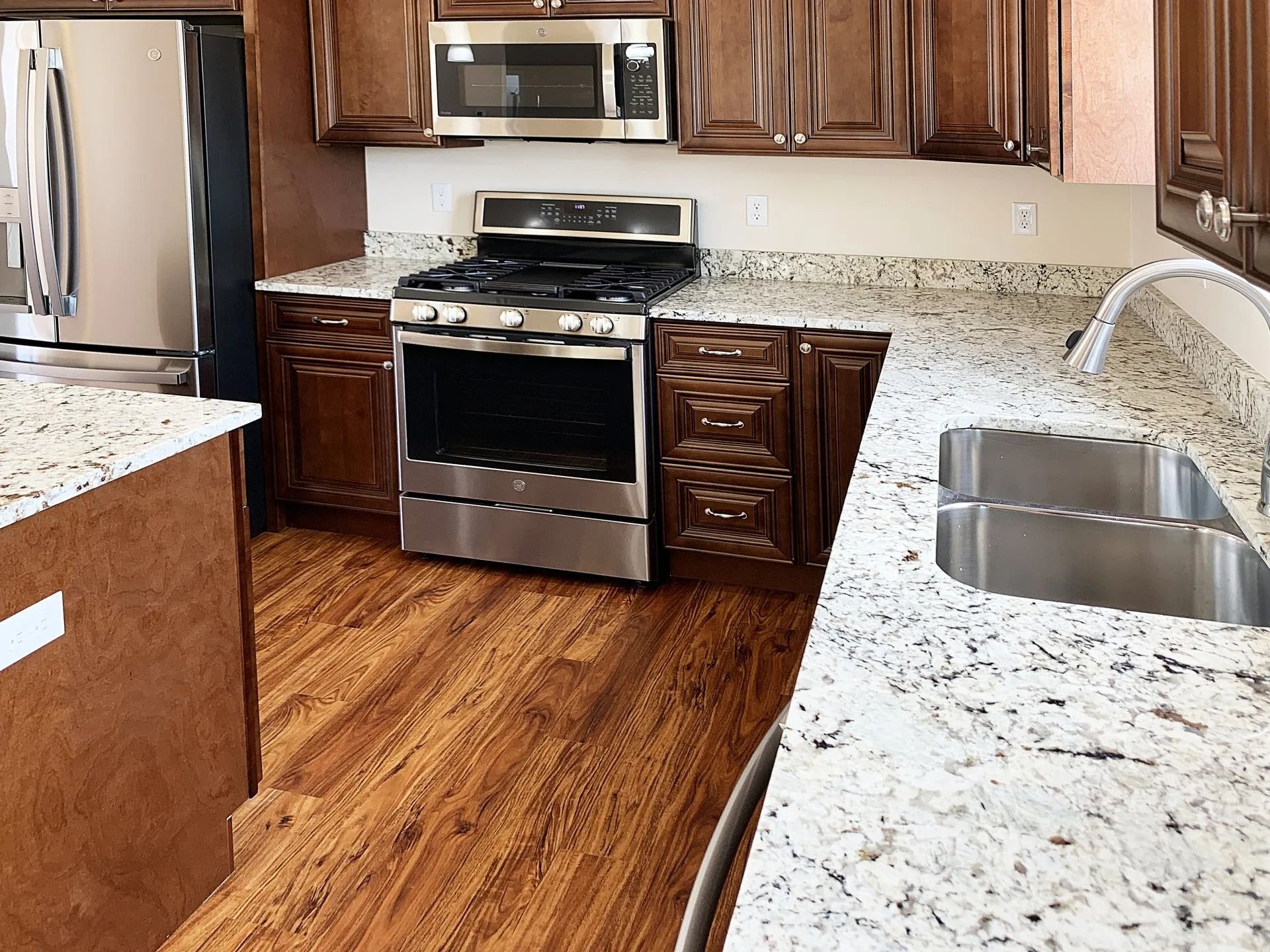 Kitchen with dark wood cabinets, granite countertops, stainless steel appliances, and wood-look flooring.