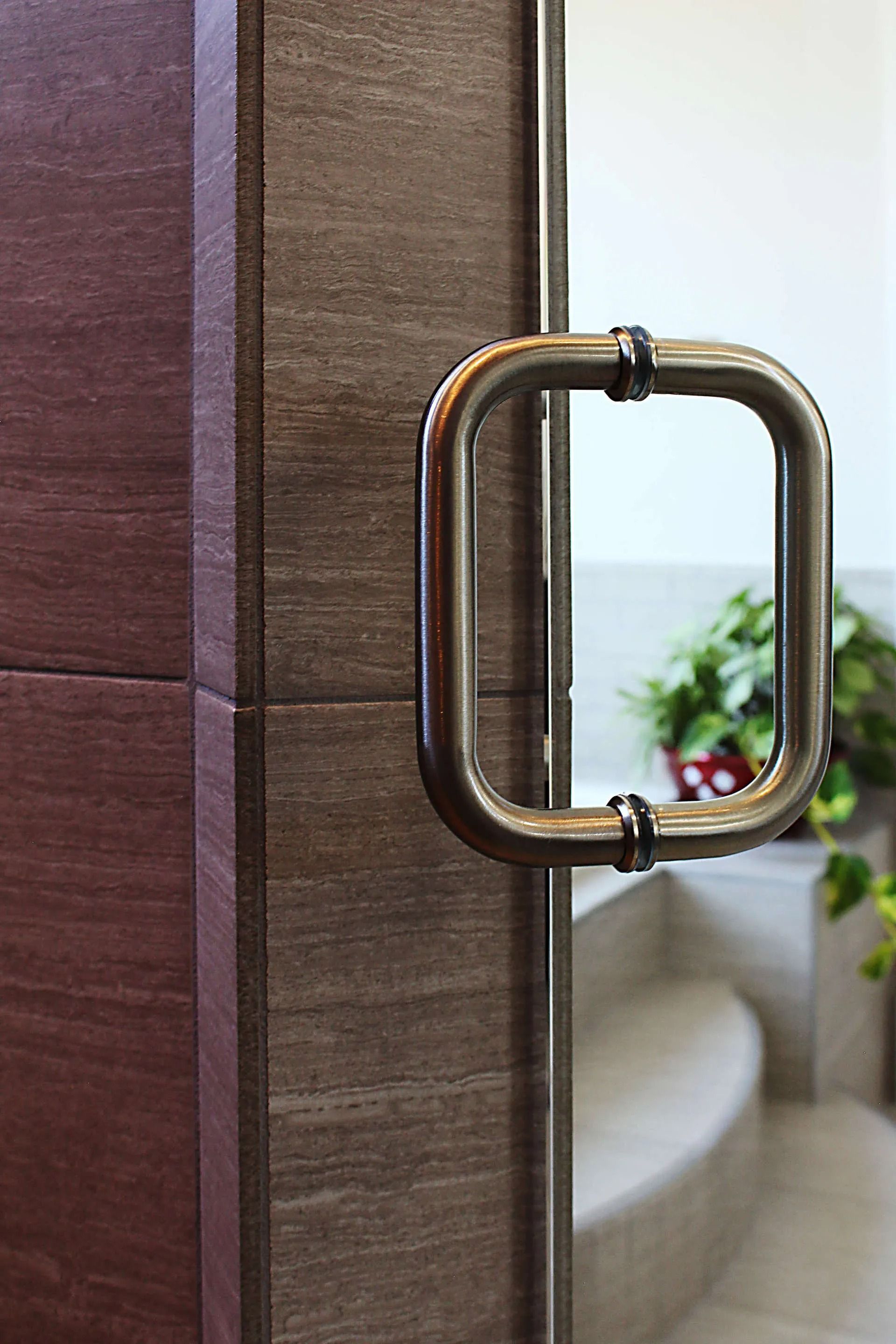 A close-up view of a rectangular, polished metal handle on a glass door against a dark, textured tiled wall.