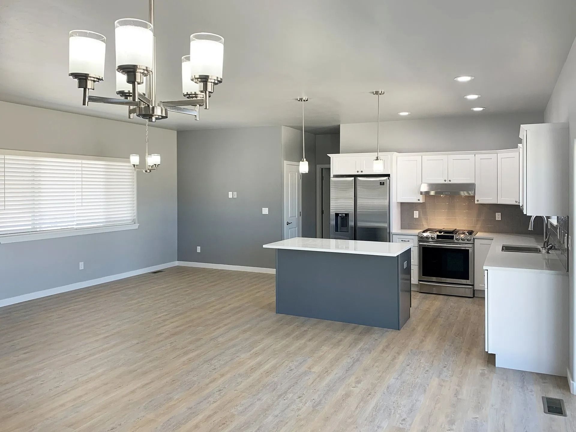 A modern open-concept kitchen and living area featuring white cabinets, a dark gray island, and a dining chandelier.