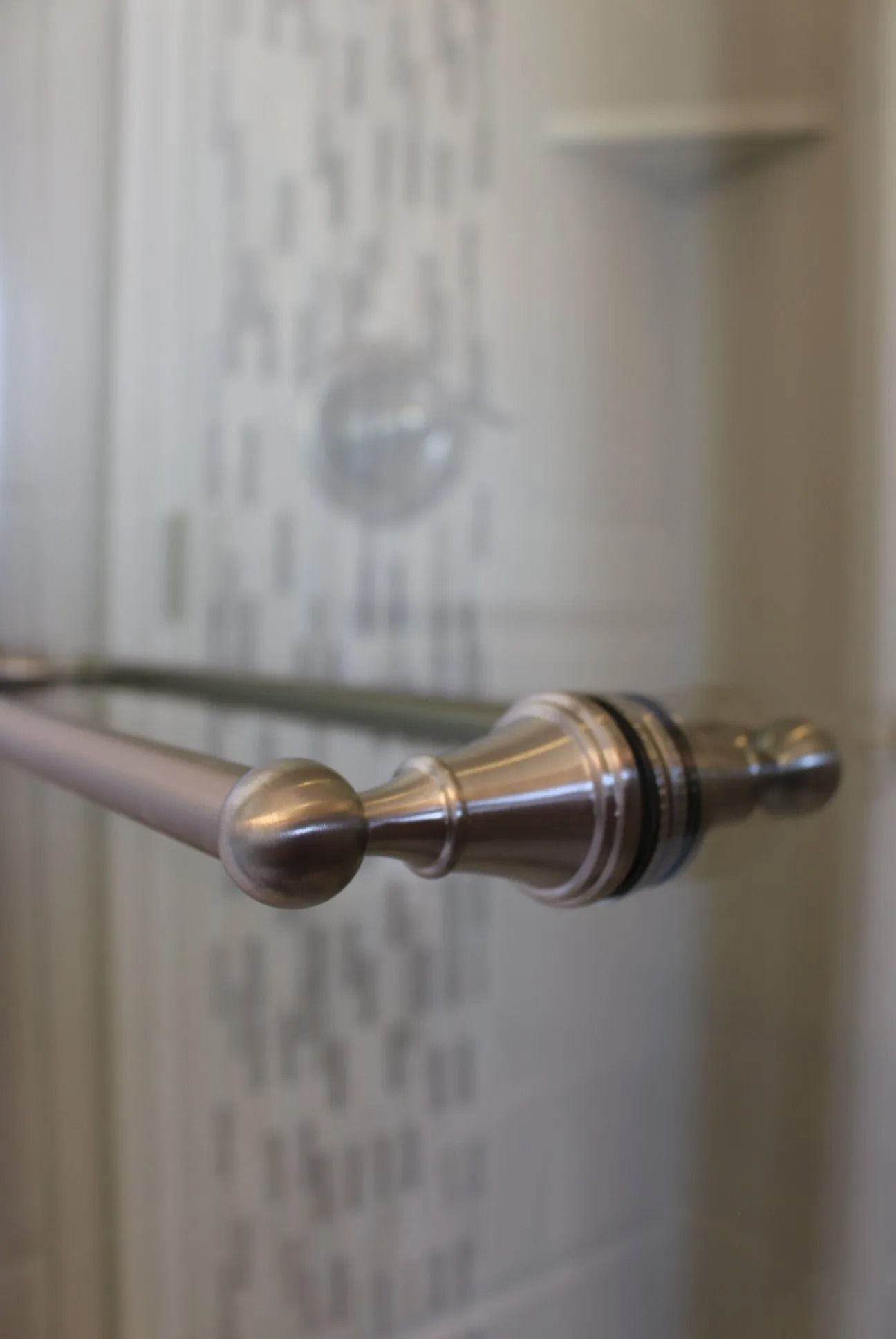 Close-up of a brushed nickel towel bar with decorative finials mounted on a tiled bathroom wall.