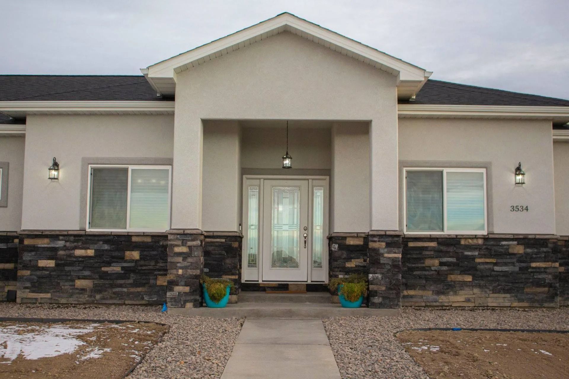 A light-colored house with a dark stone base, a gabled porch entry, and two windows on either side of a central door.
