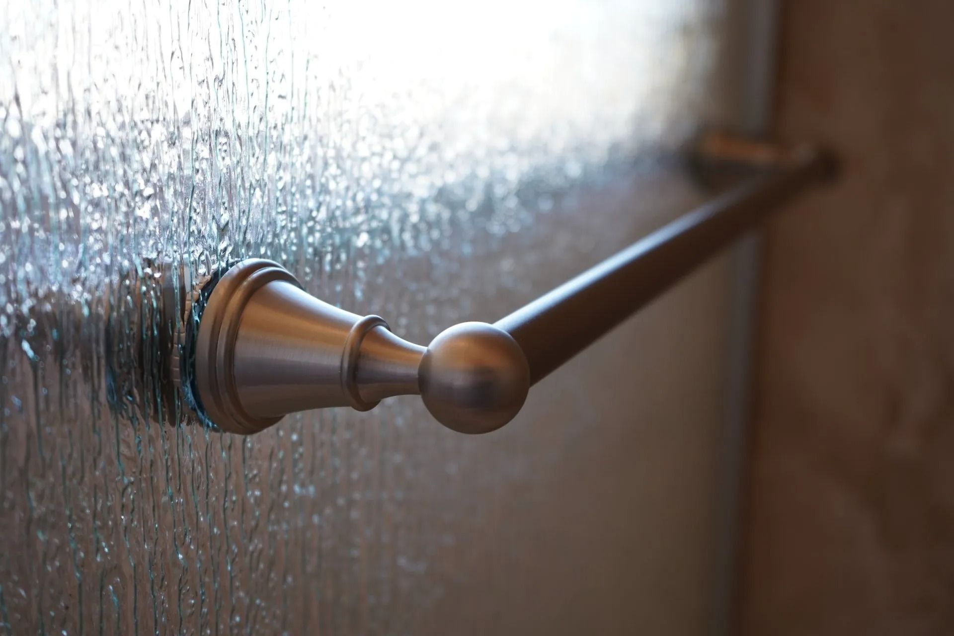 A close-up view of a brushed nickel handle on textured, rain-patterned shower glass.