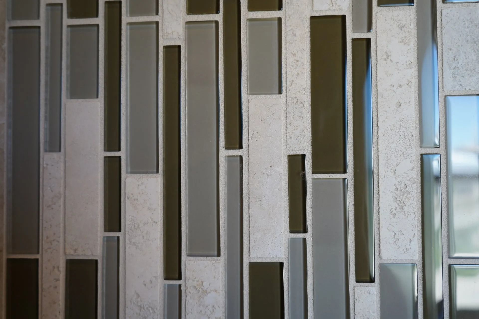 A vertical mosaic tile pattern featuring alternating strips of grey glass, dark brown glass, and textured white stone.