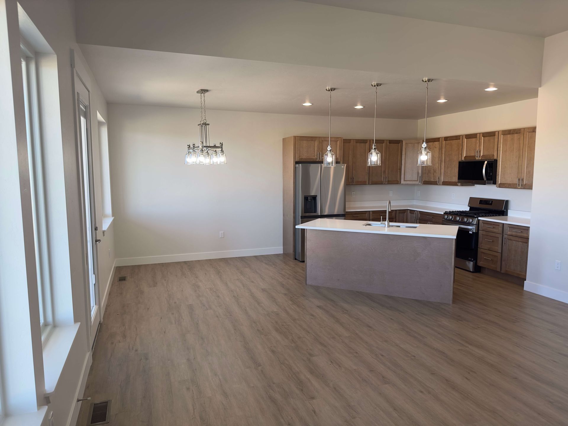 An open-concept kitchen and dining area with wood-look flooring, light-toned cabinets, an island, and pendant lighting.