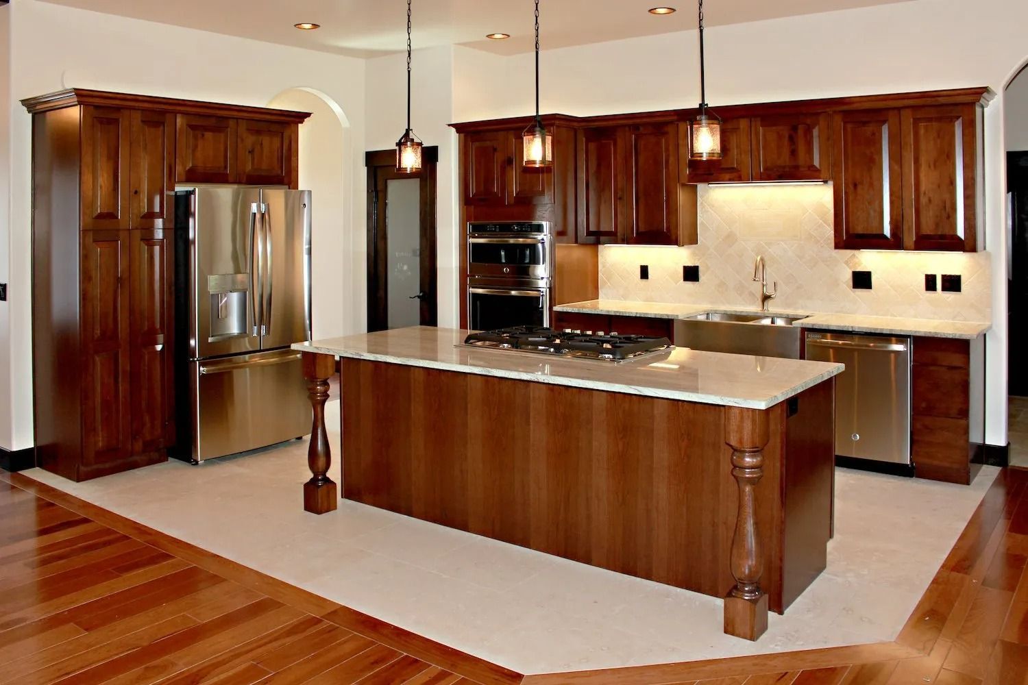 A modern kitchen with cherry wood cabinets, stainless steel appliances, a central island with a cooktop, and tile flooring.