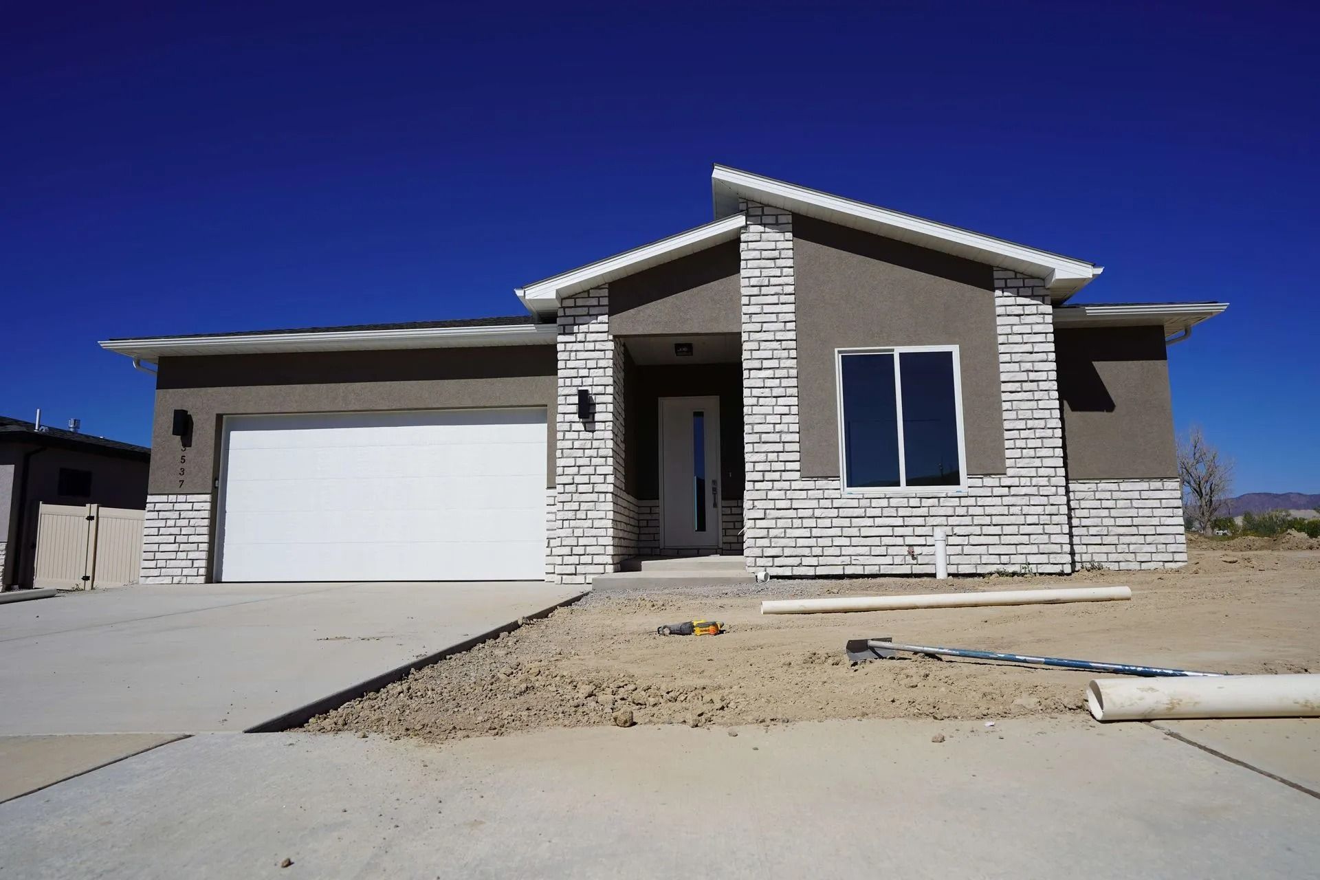 A modern one-story suburban house with a white stone and taupe exterior, a two-car garage, and a concrete driveway.