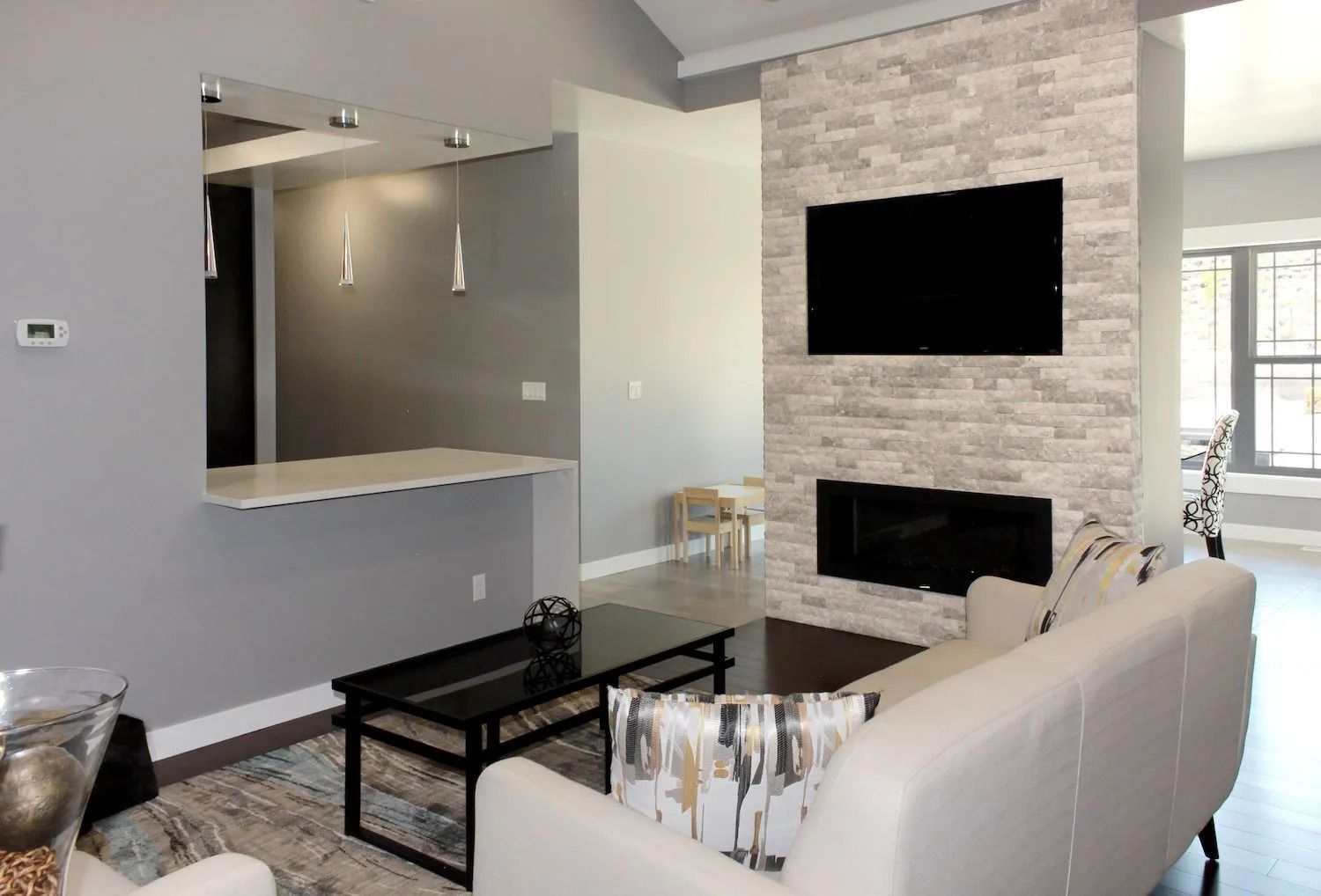 Modern living room with a stone fireplace, mounted television, a couch, a black coffee table, and a kitchen pass-through.