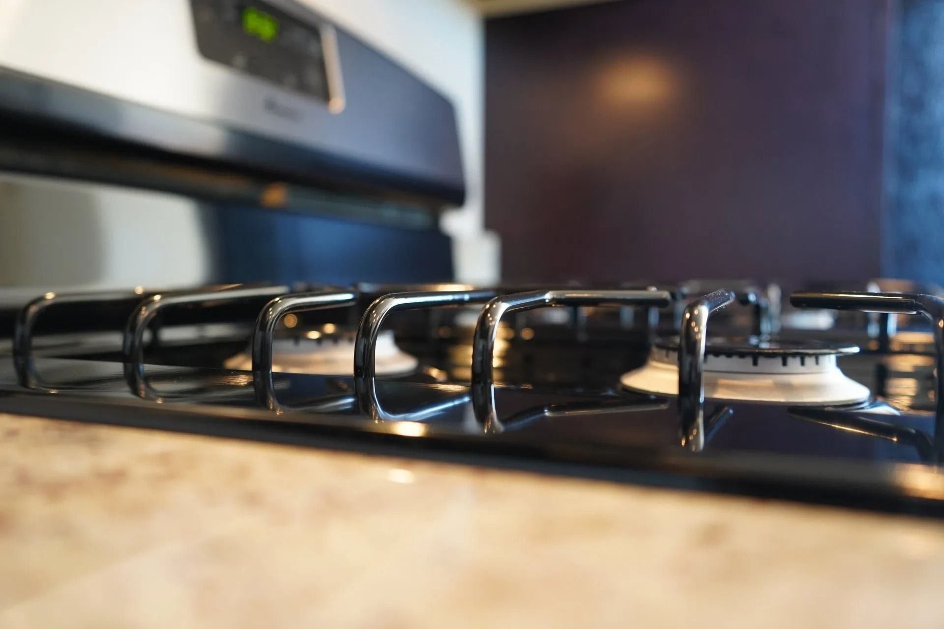 A close-up, low-angle view of a clean black gas stovetop with metal grates and a stainless steel oven control panel.