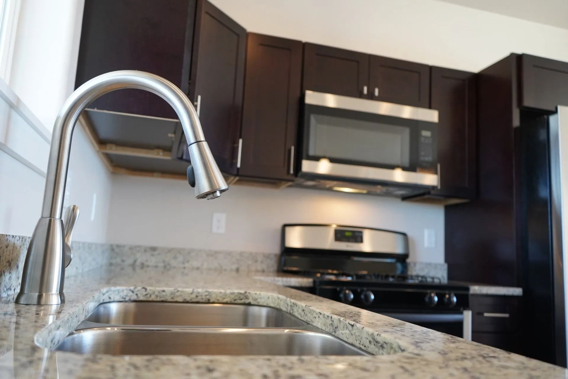 A modern kitchen with dark wooden cabinets, granite countertops, a stainless steel sink and faucet, and a range.