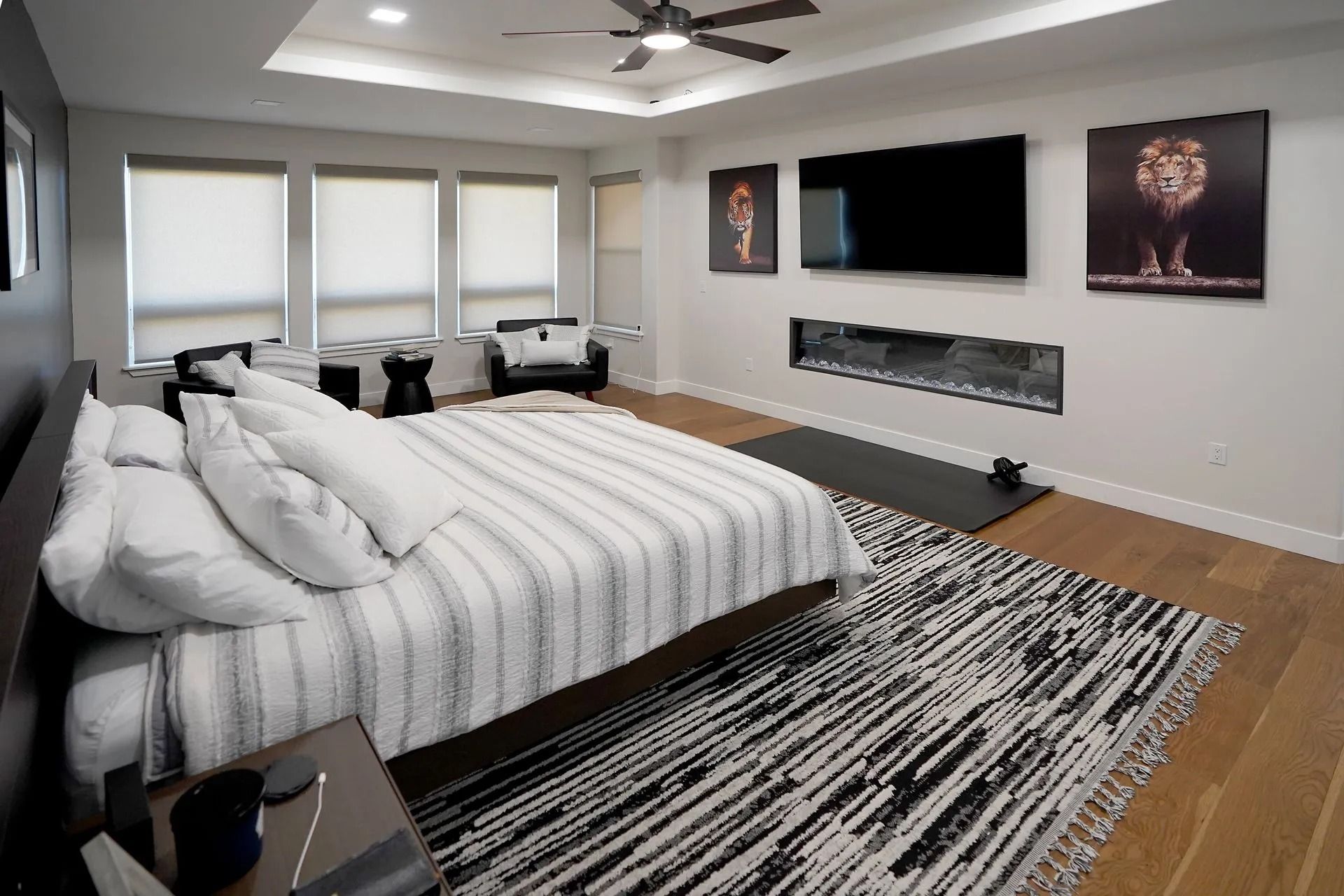 A modern bedroom featuring a bed with striped bedding, a fireplace below a wall-mounted TV, and a geometric area rug.
