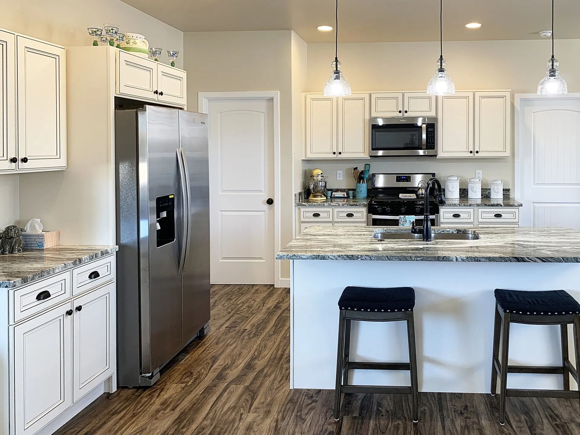 A kitchen with white cabinets, stainless steel appliances, granite countertops, and two black stools at an island.