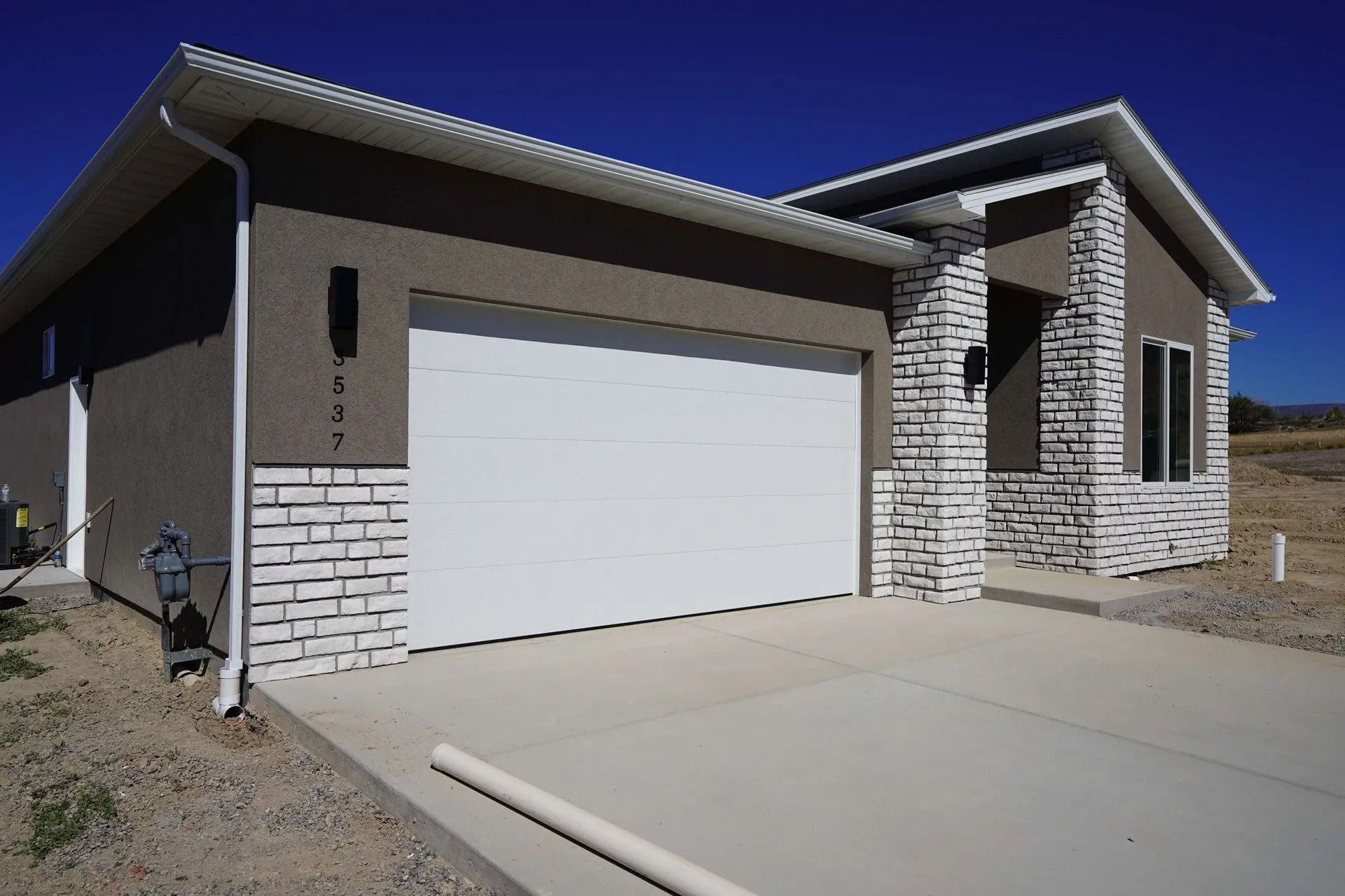 A modern one-story home with a white garage door, beige stucco walls, and white stone accents under a clear blue sky.