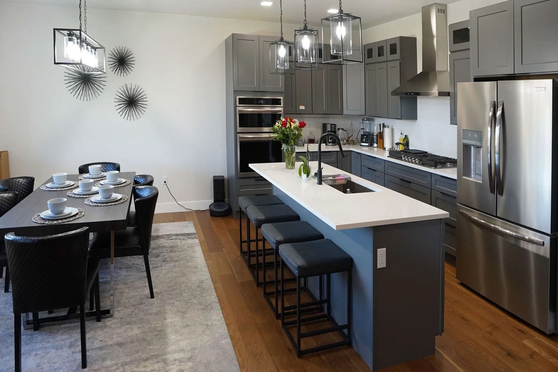 Modern kitchen and dining area with gray cabinets, stainless steel appliances, a white-topped island, and a dining table.