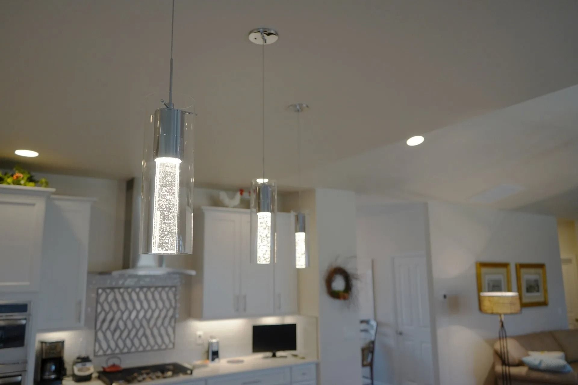 Three cylindrical pendant lights with bubble-glass details hang above a white kitchen island in an open-concept home.