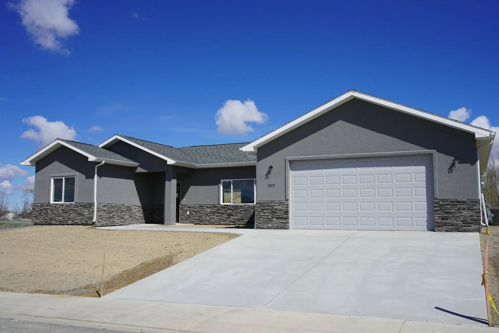 A modern, single-story, grey-stucco suburban home with a stone-veneer base and an attached two-car garage.