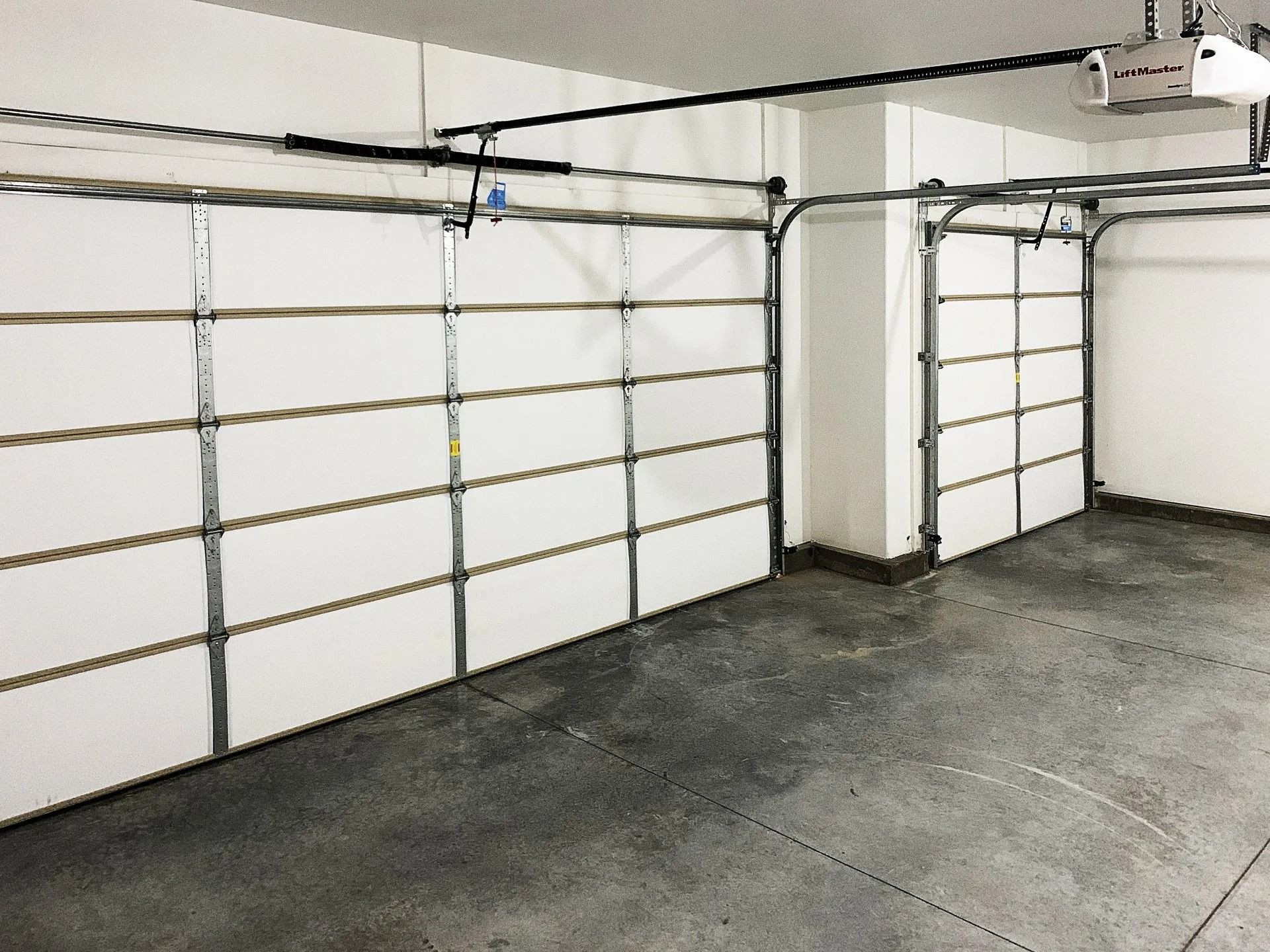 Two white sectional garage doors installed on adjacent walls in a garage with a concrete floor.