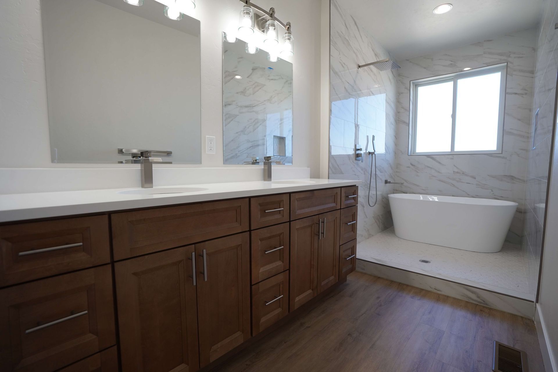 Modern bathroom with dark wood vanity, white countertop, large mirror, and freestanding tub by a window