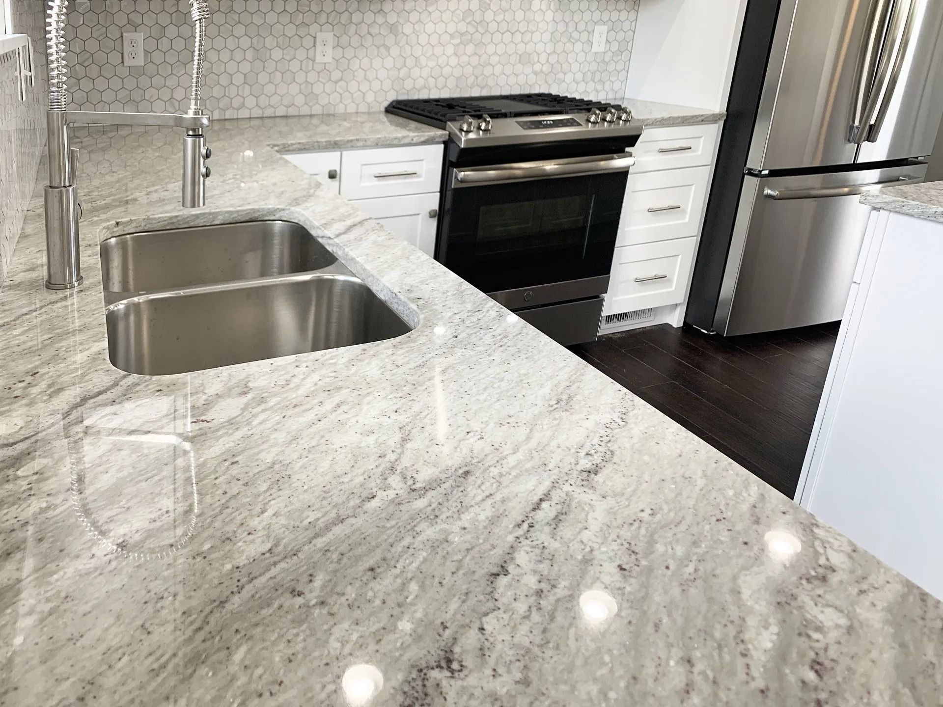 A kitchen featuring white cabinets, a light-colored granite countertop with a double sink, and stainless steel appliances.