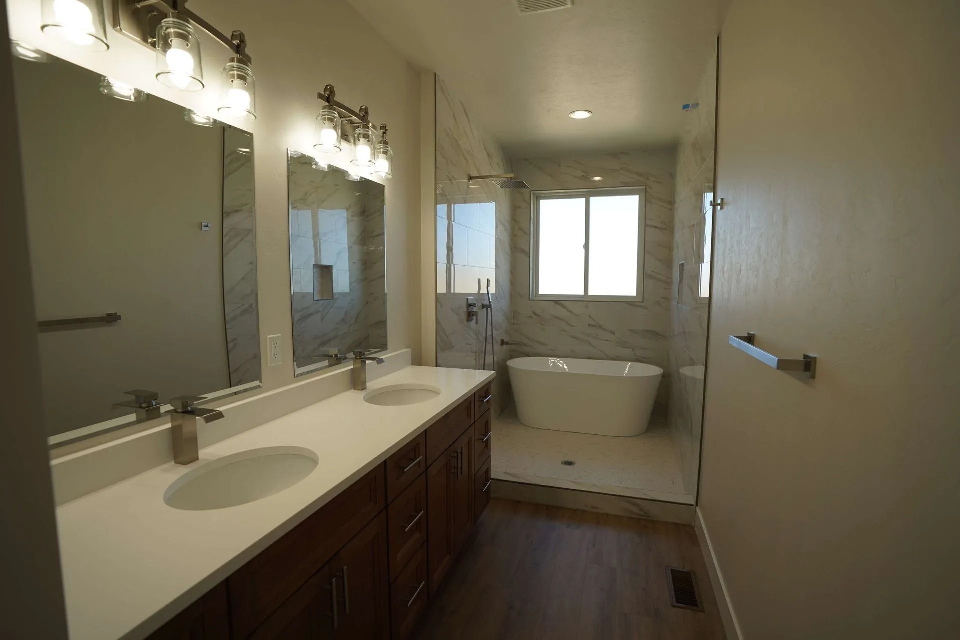 Modern bathroom with dual vanity, wood cabinets, marble counters, a freestanding tub, and shower in a wet room.