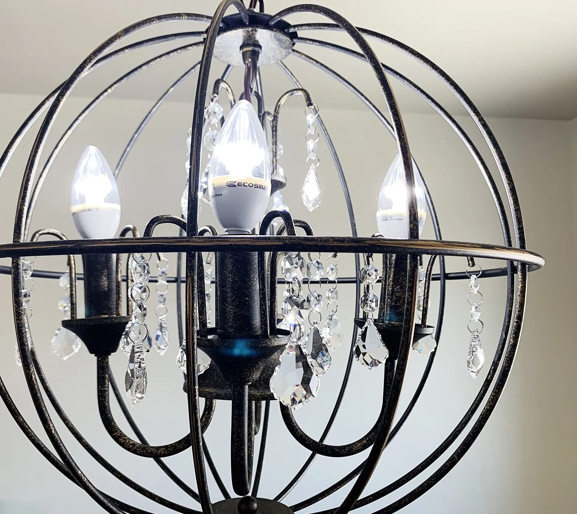 A dark metal, spherical chandelier with exposed candelabra light bulbs and dangling crystal accents.