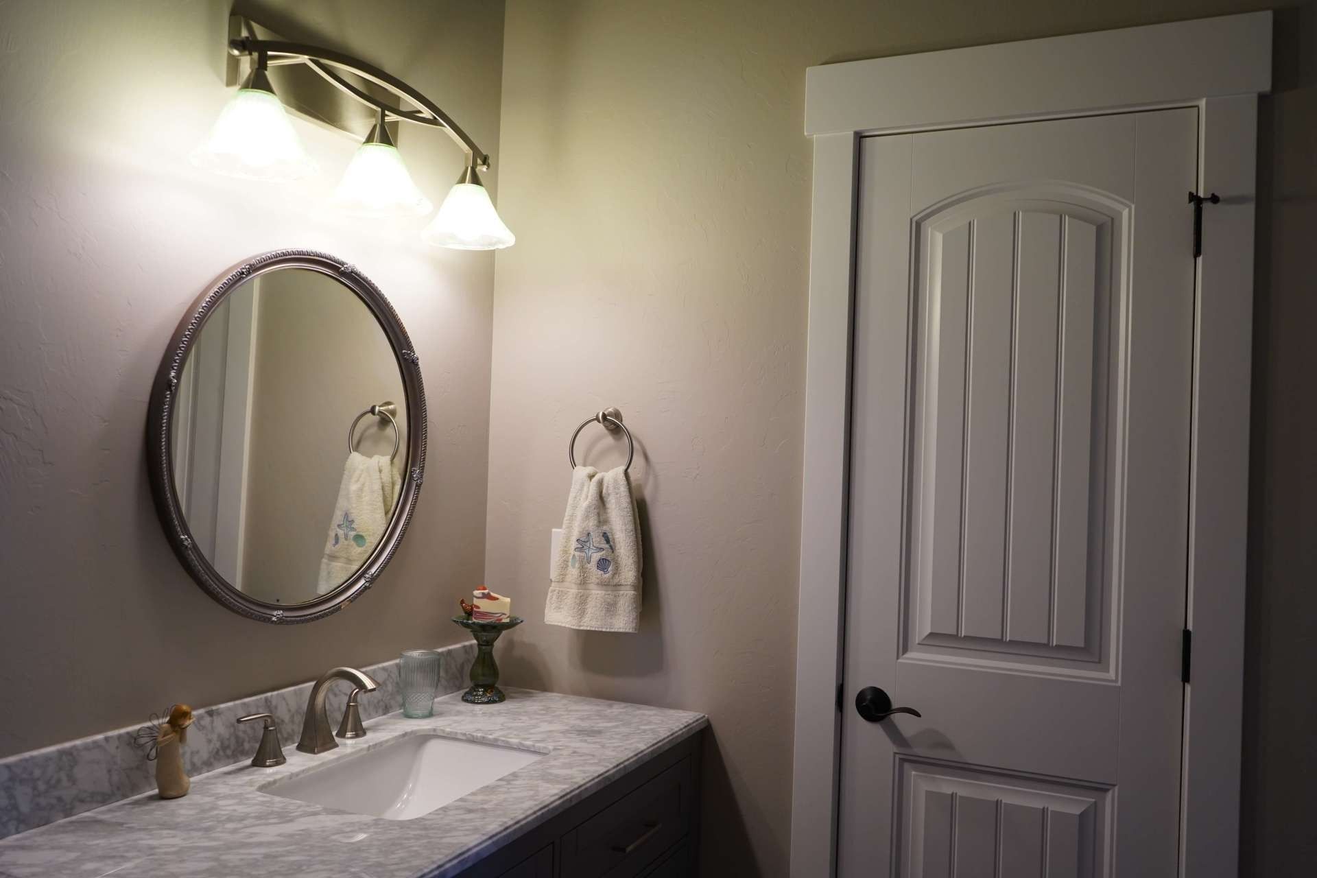 A bathroom vanity with a circular mirror, wall-mounted lights, and a white door to the right.