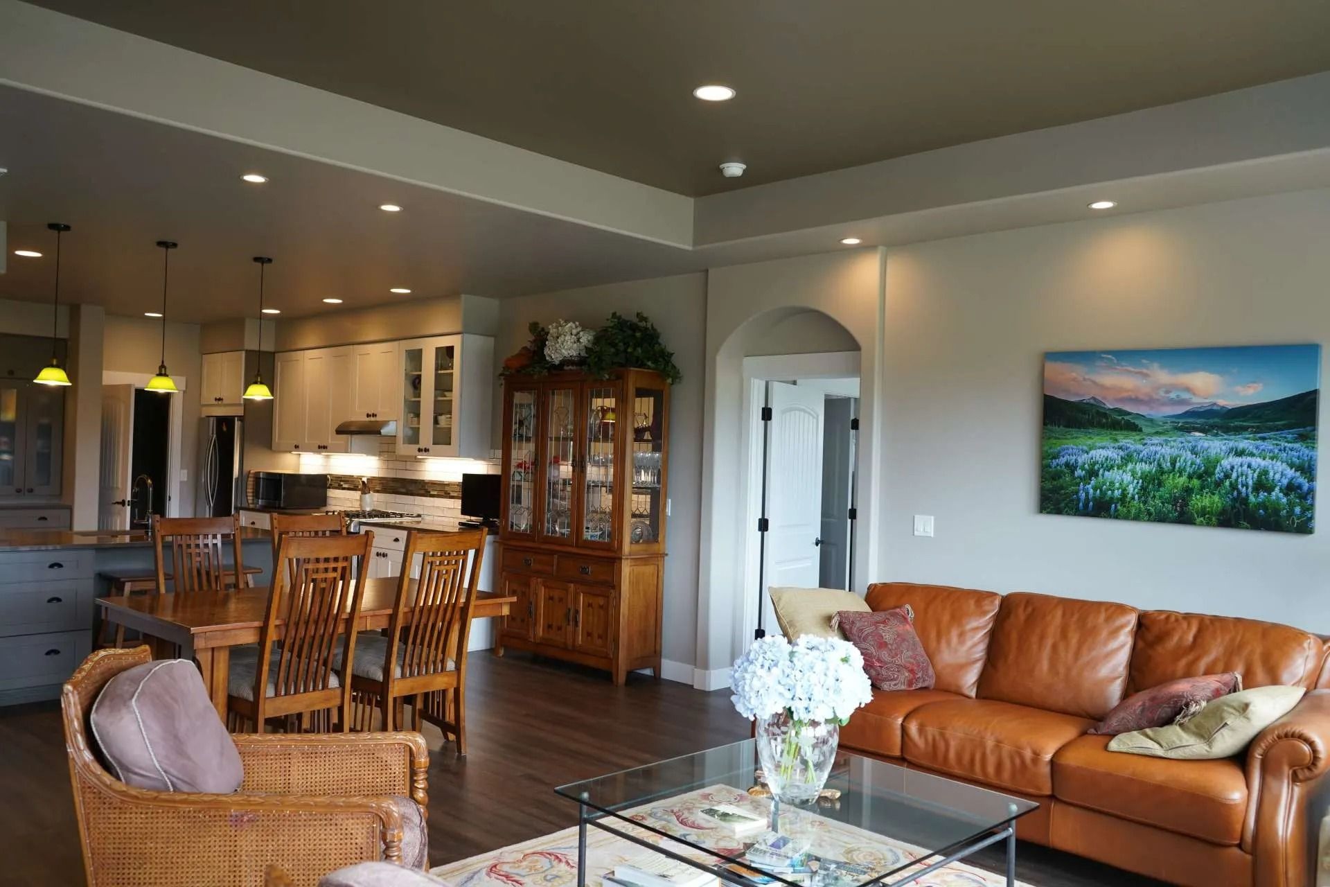 A brown leather sofa, wicker chair, and dining set in an open-concept living area with neutral walls and wood flooring.
