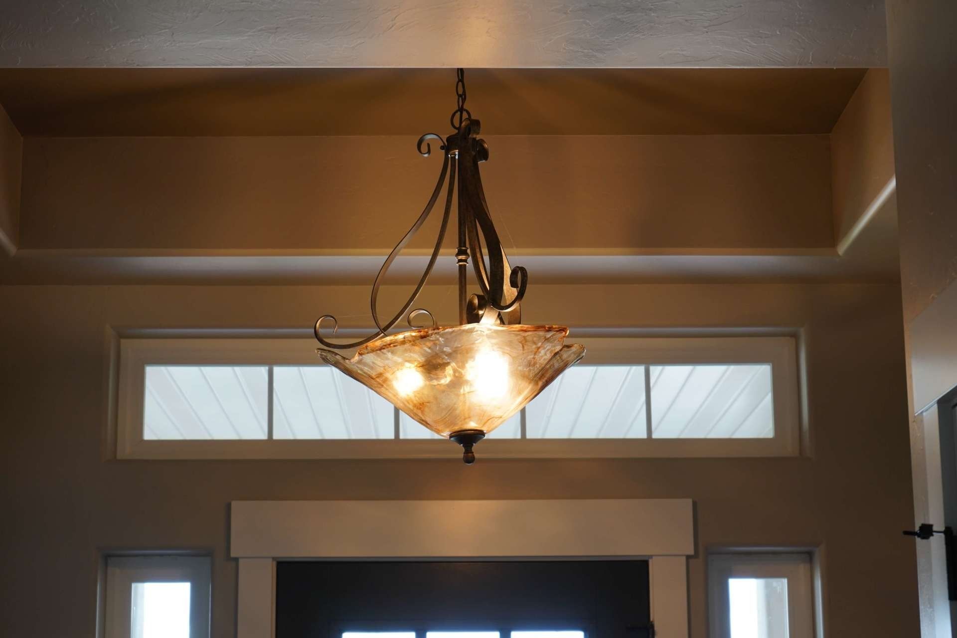 A decorative metal chandelier with a frosted glass bowl hangs from a tray ceiling above a entryway.