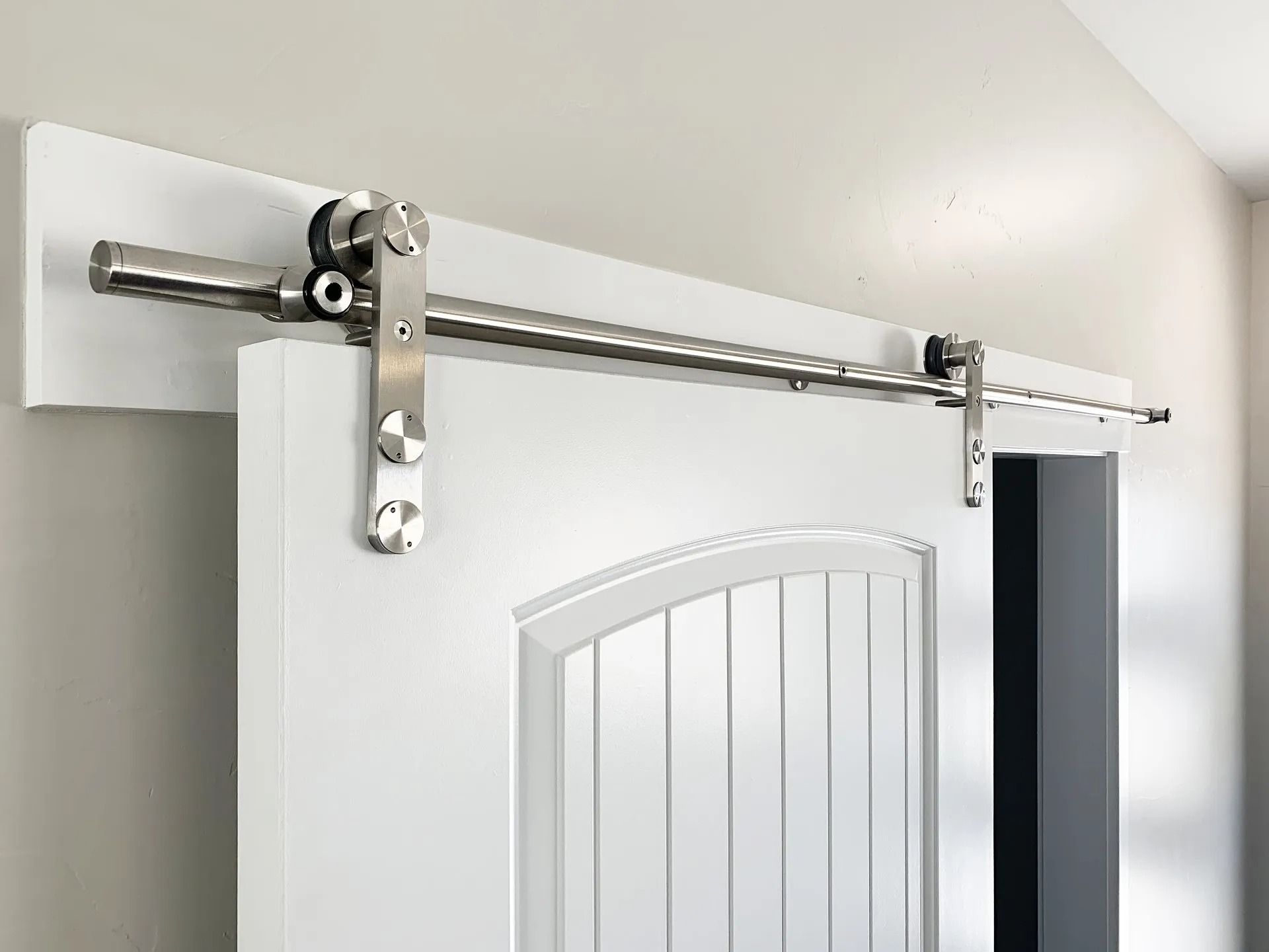 A stainless steel barn door hardware kit installed on a white door and a white wooden header board.