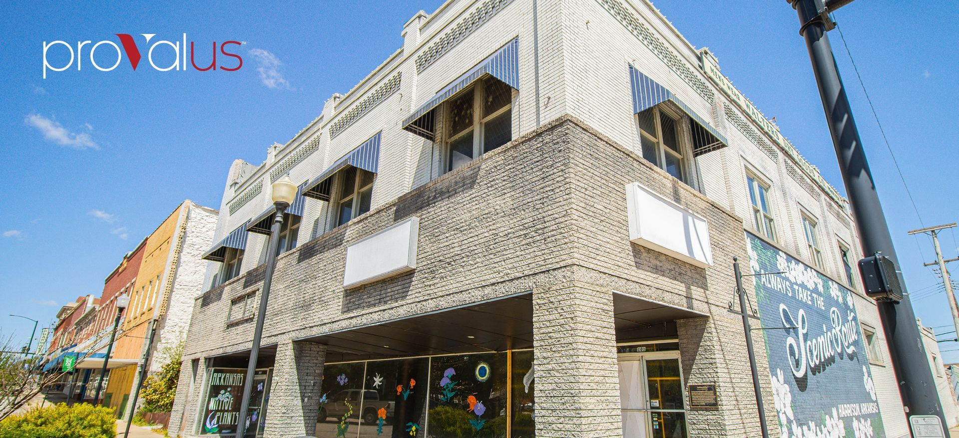 Corner view of a white brick building with storefront windows on a sunny street under blue sky