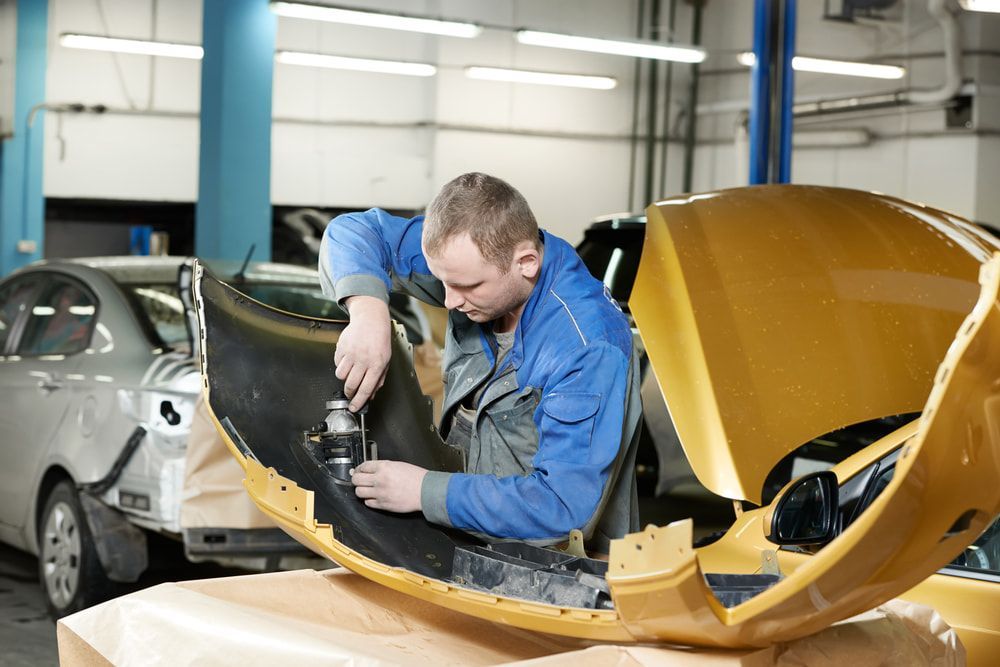 A Man Is Working On A Yellow Car In A Garage — Taminda Smash Repairs In Tamworth, NSW