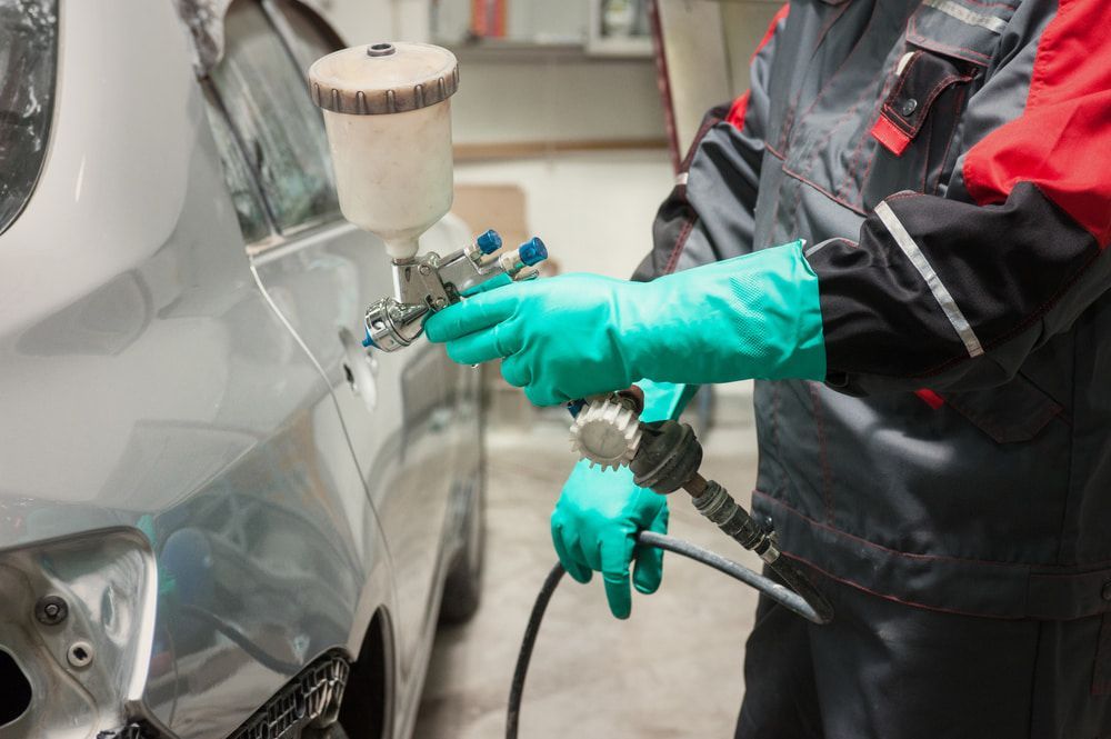 A Man Is Spraying Paint On A Car In A Garage — Taminda Smash Repairs In Taminda, NSW