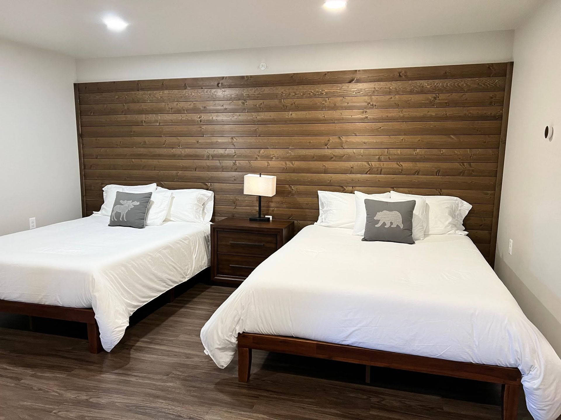 Two beds with white linens, a nightstand, and a wood accent wall in a bedroom.