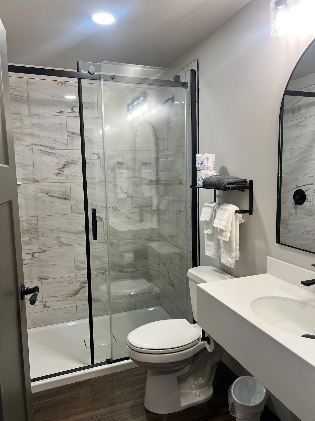 Modern bathroom with glass shower, white vanity, toilet, and black fixtures.