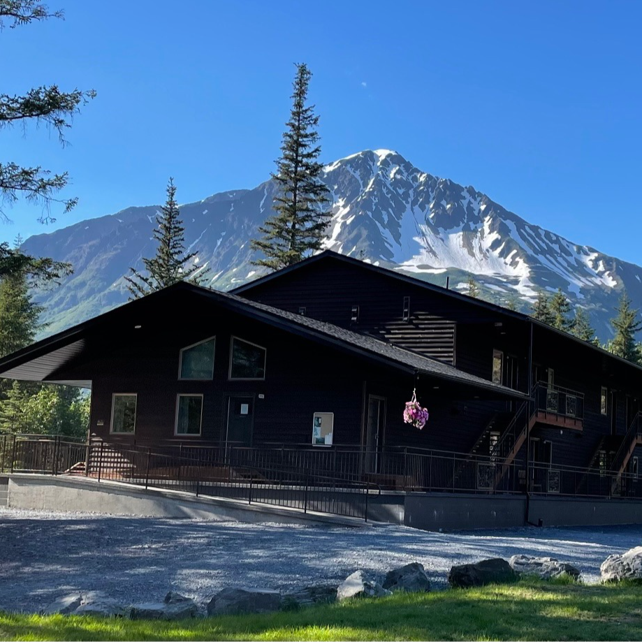 Black lodge with mountain backdrop, ramp access, sunny day.
