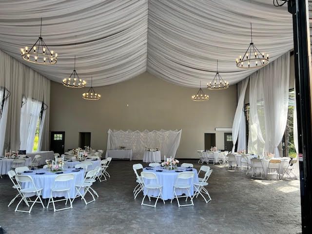 Empty event space with round tables set for a gathering, white linens, and decorative lighting.