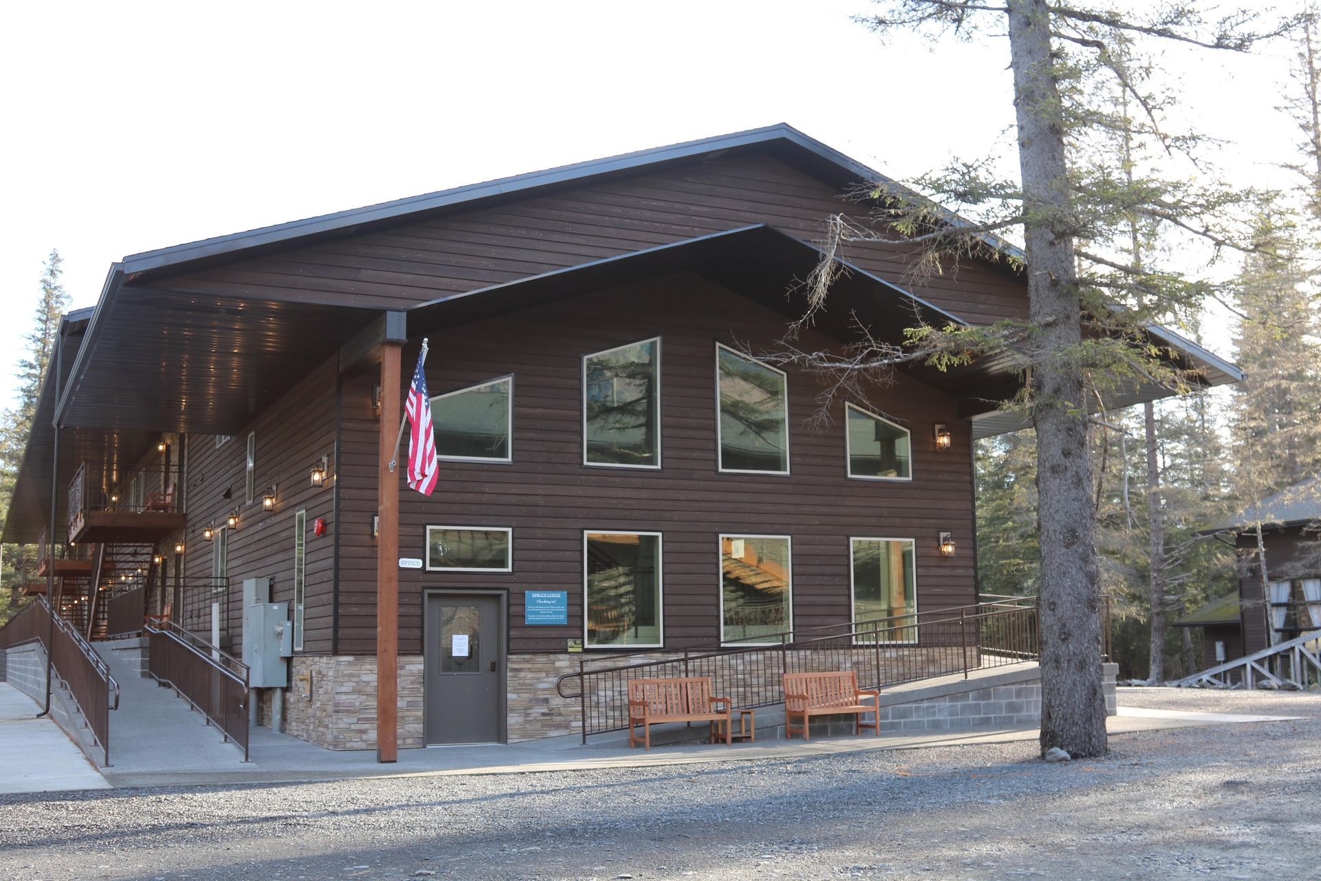 Brown building with a ramp, American flag, and benches.