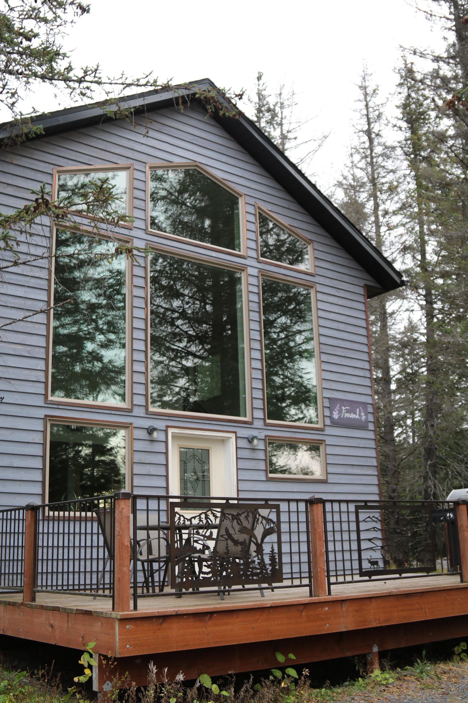 Gray cabin with large windows and a small deck; surrounded by trees.