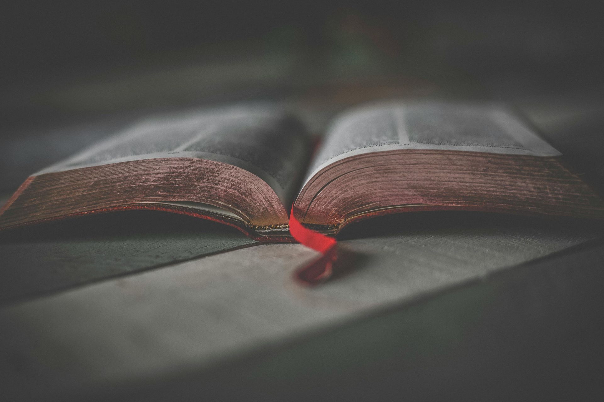 Open book with a red ribbon bookmark on a neutral-toned surface, soft lighting.