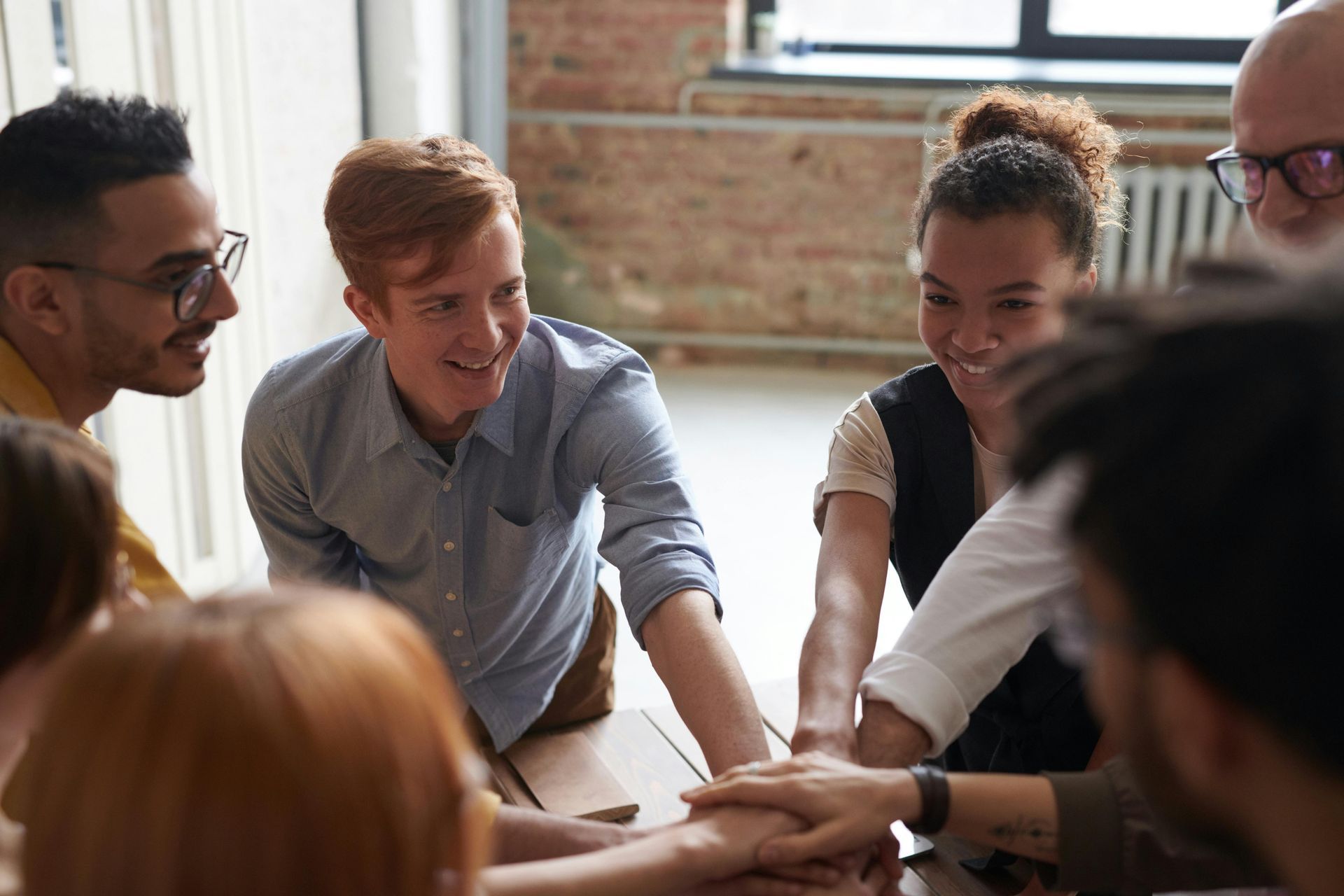 Group of diverse people, hands stacked together in a meeting, smiling, in a modern office.