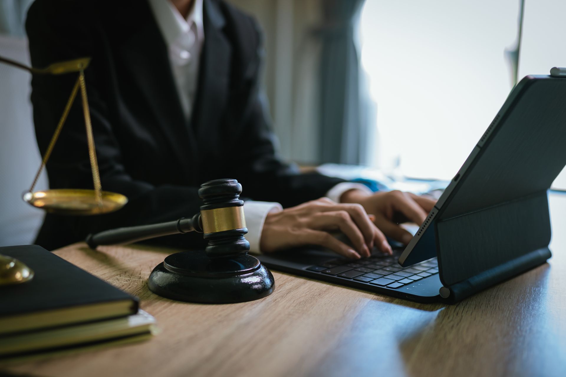 Attorney working on a laptop beside a gavel and scales of justice on an office desk. Attorney working on a laptop beside a gavel and scales of justice on an office desk.