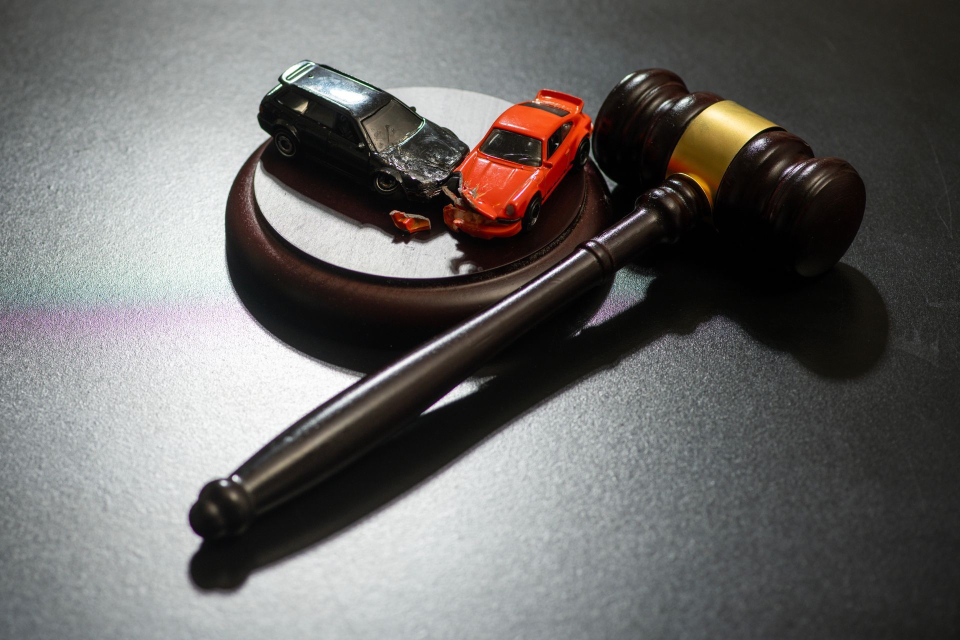 a wooden judge’s gavel beside two toy cars on a dark surface.