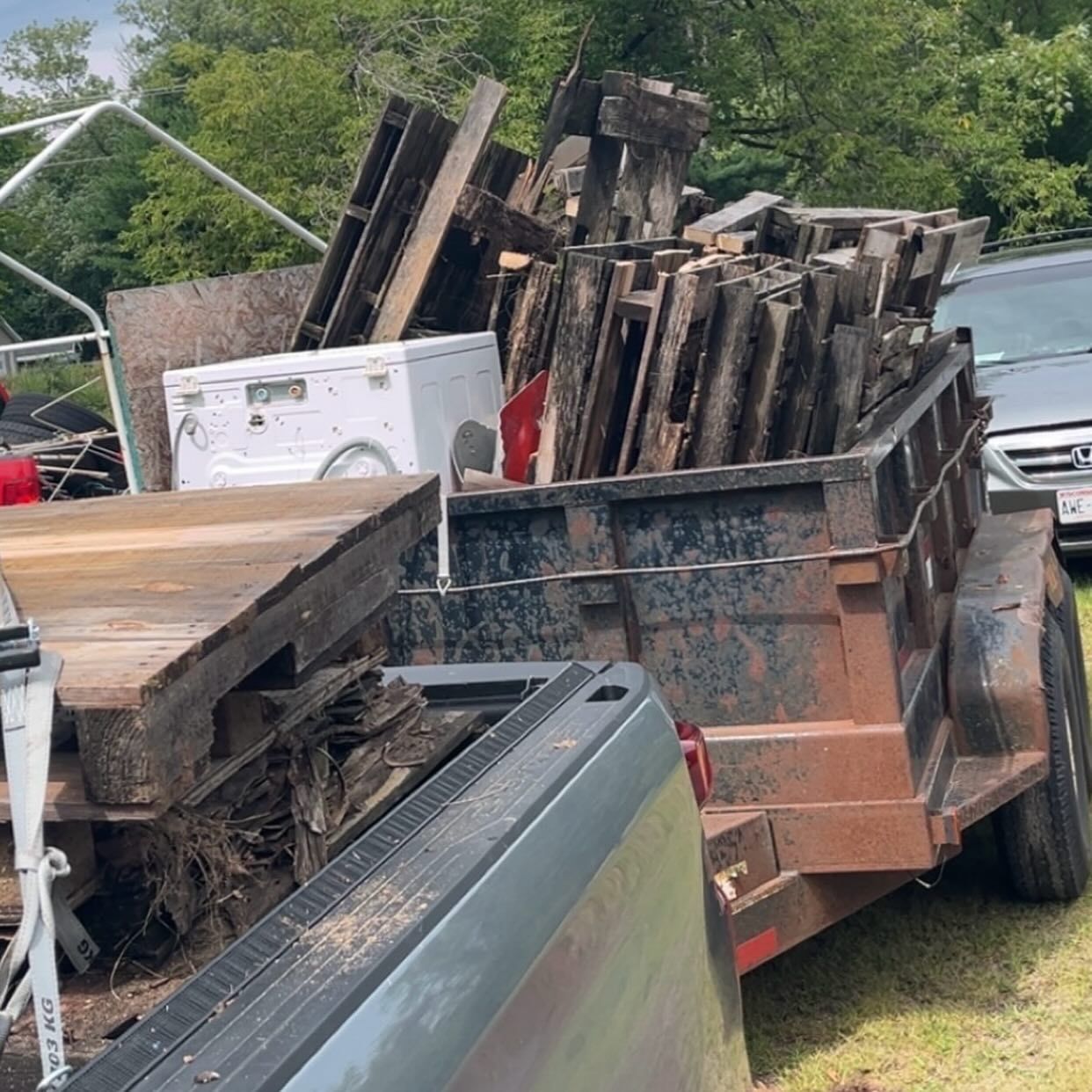 Rusted trailer loaded with charred wooden debris and scrap in a grassy yard